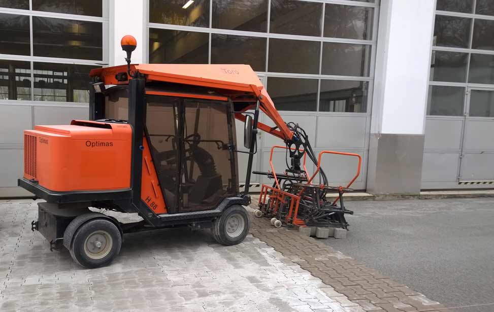 Eine Optimas Pflasterverlegemaschine beim Einsetzen einer Lage Pflastersteine in eine Verlegeschicht aus Splitt.